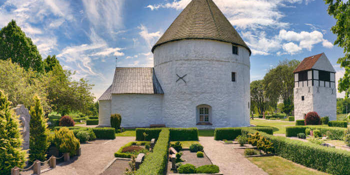 Rundkirche auf der Insel Bornholm, Dänemark, mit weiß verputzten Mauern, kegelförmigem Dach und gepflegtem Garten bei blauem Himmel.