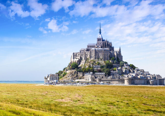 Busreisen nach Frankreich. Mont-Saint-Michel in der Normandie, Frankreich, auf einer Felseninsel mit Abtei und Stadtmauern, umgeben von Salzwiesen unter blauem Himmel.