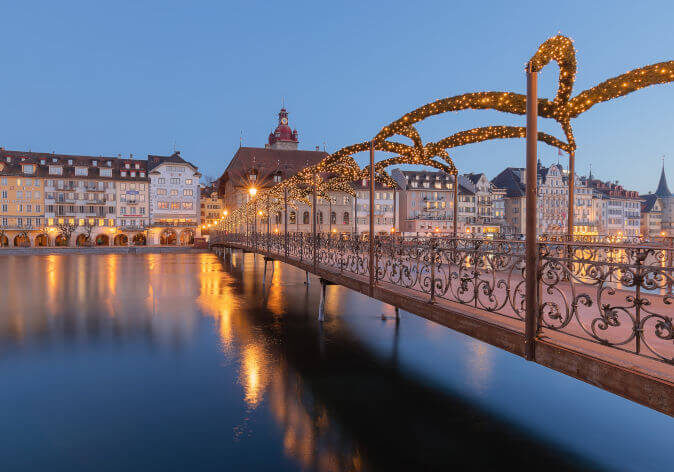 Festlich geschmückte Altstadt von Luzern im Advent mit Lichterketten, Weihnachtsmarktständen und Blick auf die Kapellbrücke bei Abenddämmerung.