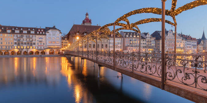 Festlich geschmückte Altstadt von Luzern im Advent mit Lichterketten, Weihnachtsmarktständen und Blick auf die Kapellbrücke bei Abenddämmerung.