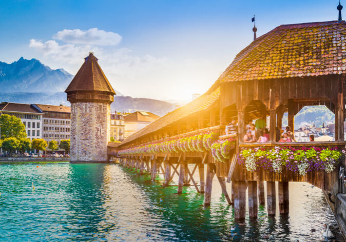 Luzern Schweiz Reisen. Kapellbrücke mit Wasserturm in Luzern, Schweiz, bei Sonnenuntergang und blumengeschmücktem Geländer über der Reuss.
