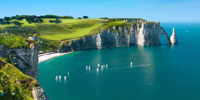 Kreidefelsen von Étretat an der Alabasterküste in der Normandie, Frankreich, mit blauem Meer und grünen Wiesen an einem sonnigen Tag.