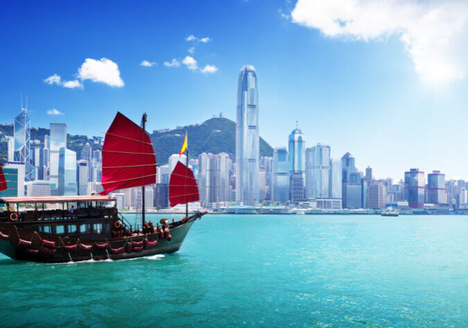 Reisen nach China. Dschunke mit roten Segeln in der Victoria Harbour Bucht vor der Skyline von Hongkong, China