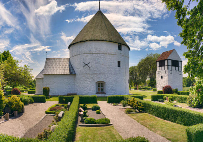 Reisen Ostsee, Reisen zur Insel Bornholm. Weiße Rundkirche mit gepflegtem Garten auf der Insel Bornholm, Dänemark, unter blauem Himmel mit leichten Wolken.