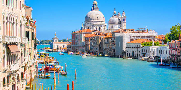 Grand Canal in Venedig, Italien, mit der Kirche Santa Maria della Salute und historischen Palästen bei blauem Himmel.