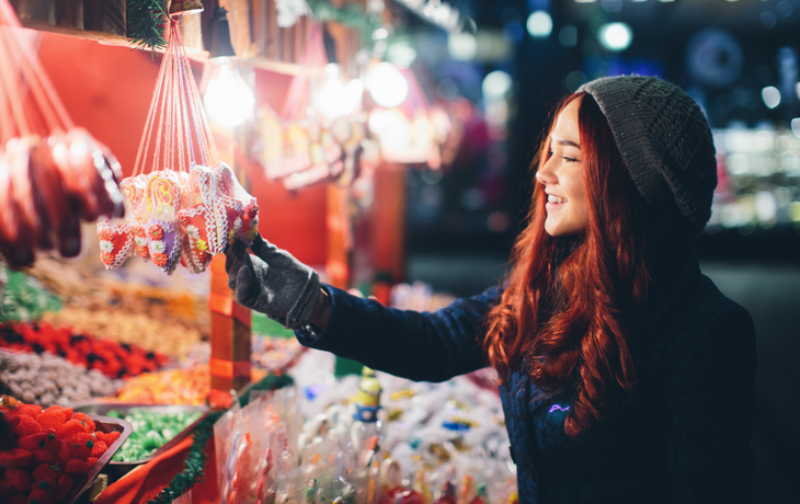 junge Frau kauft abends Süßigkeiten auf dem Weihnachtsmarkt
