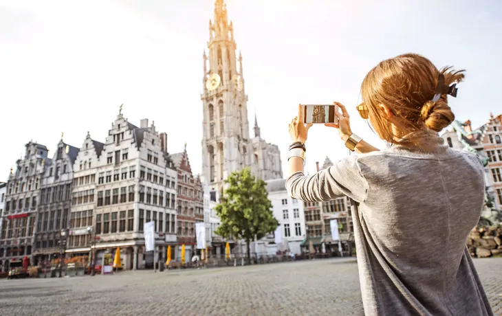 Young woman tourist photographing with phone famous cathedral standing on the Great Market square during the morning in Antwerpen, Belgium